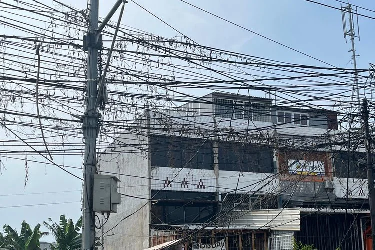 Kondisi jaringan kabel utilitas di kawasan Jalan Peta Barat, Pegadungan, Kalideres, Jakarta Barat, tampak sangat semrawut dan dibiarkan tidak terawat, Kamis (25/6/2026)