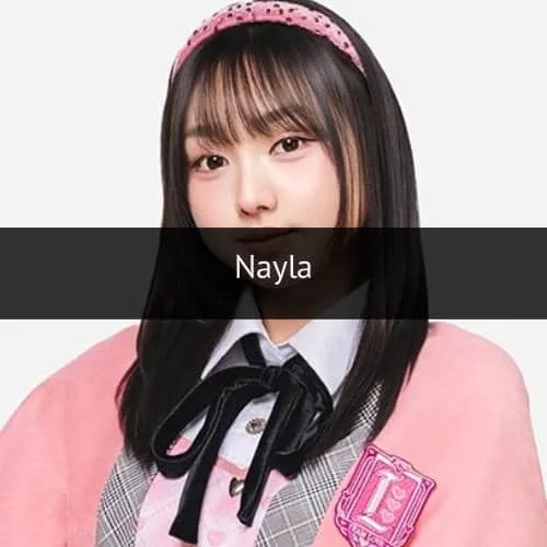 Seorang anggota grup idola mengenakan seragam berwarna pink dan abu-abu dengan pita hitam serta bando pink di rambutnya.