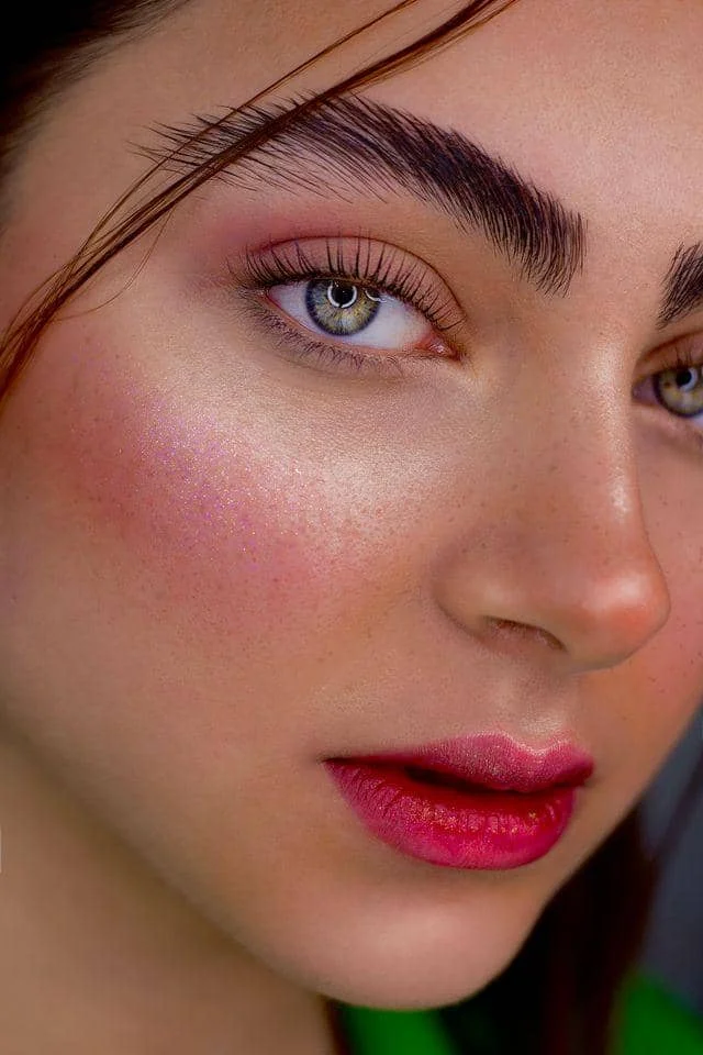 Wajah perempuan dengan riasan blush berwarna merah muda segar, kulit bercahaya, dan bibir berwarna merah alami.