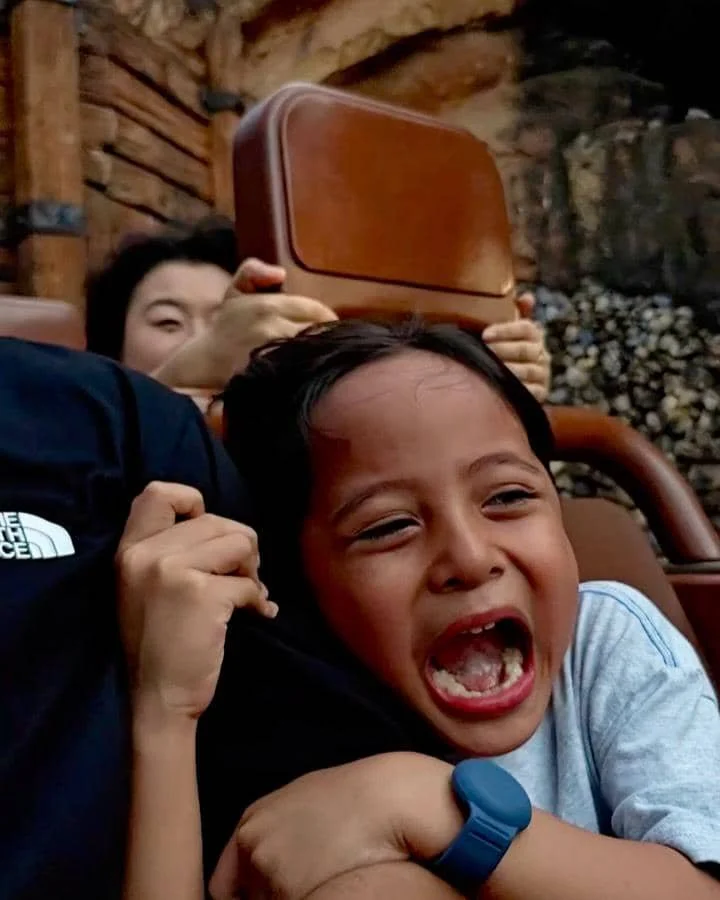 Seorang anak kecil berteriak sambil memegang erat orang dewasa saat menaiki wahana di taman bermain Disneyland Hong Kong.