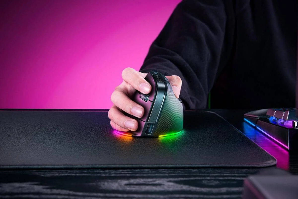 Seseorang menggunakan mouse vertikal dengan pencahayaan RGB di atas alas mouse hitam dengan latar belakang berwarna ungu muda.