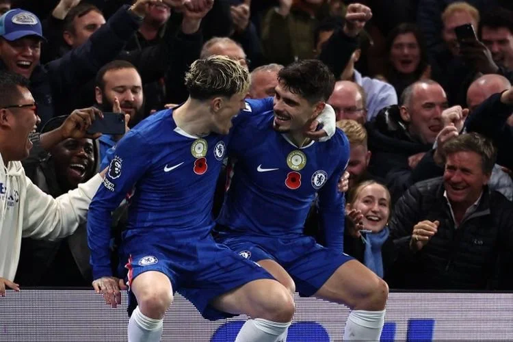Pedro Neto (kanan) duduk di papan iklan dengan Alejandro Garnacho (kiri) saat merayakan gol dalam pertandingan sepak bola Liga Inggris antara Chelsea vs Wolverhampton Wanderers di Stamford Bridge di London pada 8 November 2025. (Foto oleh HENRY NICHOLLS / AFP)