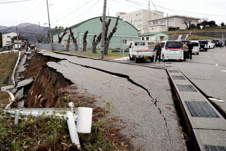 Korban gempa Jepang berdiri di samping retakan besar di trotoar setelah dievakuasi ke jalan di kota Wajima, Prefektur Ishikawa pada 1 Januari 2024.
