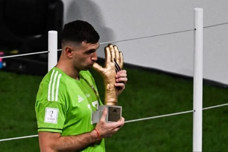Emiliano Martinez Kiper Terbaik Piala Dunia 2022. Kiper timnas Argentina, Emiliano Martinez, mencium trofi Golden Glove sebagai tanda kiper terbaik Piala Dunia 2022 Qatar. Martinez tampil gemilang pada laga Argentina vs Perancis di Stadion Lusail, Minggu (18/12/2022) malam WIB. Argentina juara usai menang adu penalti 4-3 atas Perancis. (Photo by Jewel SAMAD / AFP)